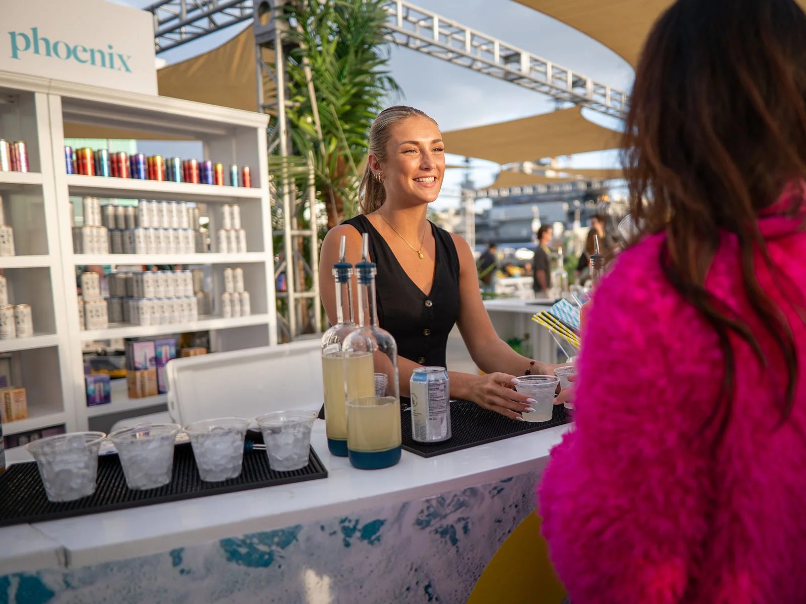 A smiling bartender serves a guest at an outdoor bar.