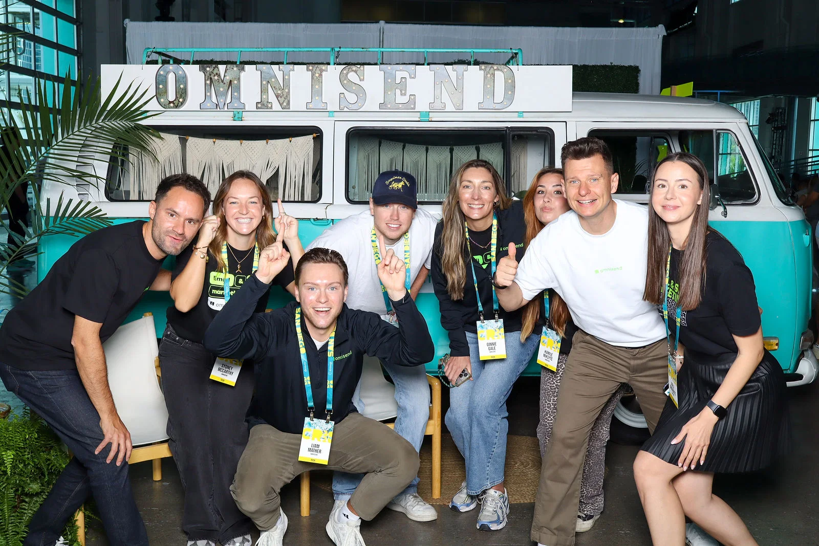 A group of smiling attendees poses together in front of a turquoise vintage van.