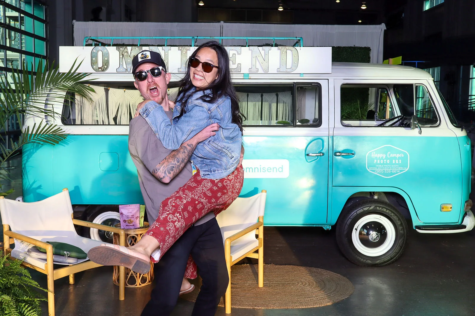 Two attendees in sunglasses embrace and smile beside a turquoise vintage van.