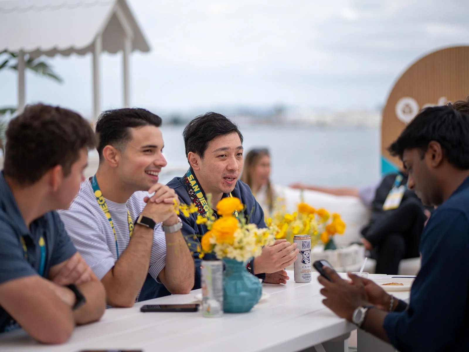 Three attendees laugh together while talking at a waterfront table with yellow flowers.